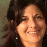 Close-up portrait of a smiling individual with long dark hair against a neutral, softly blurred background.